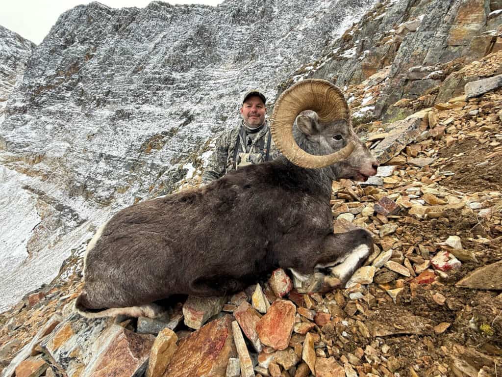 Man with a ram he hunted on a rugged mountain slope.