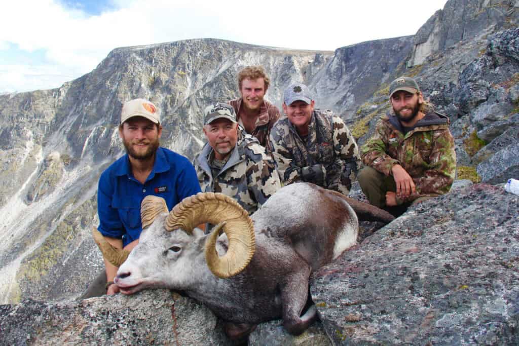 Group of hunters with mountain ram in rugged mountain landscape.