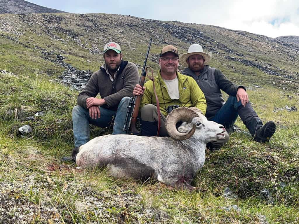 Outdoor hunters with ram trophy, scenic mountain landscape, wildlife hunting, trapper's gear.