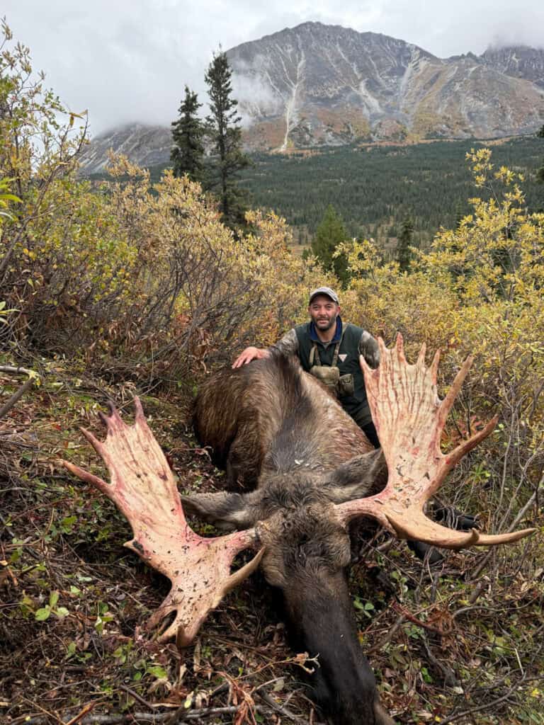 Hunter with moose after successful hunt in scenic wilderness setting.