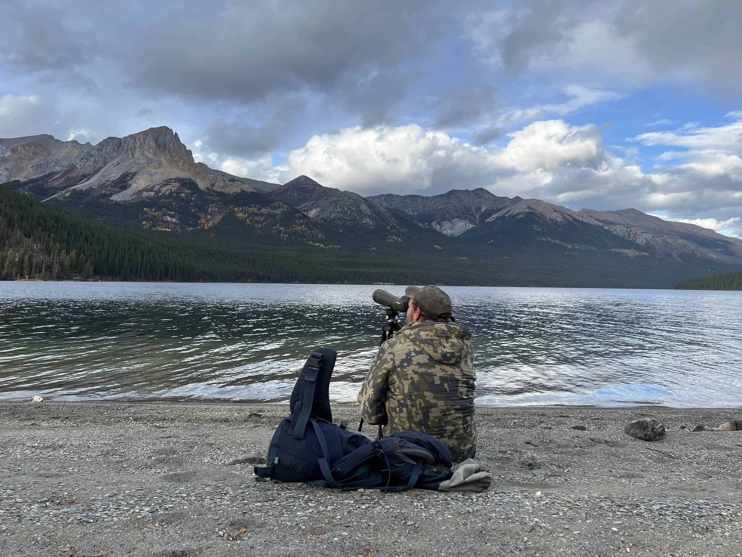 Scenic mountain lake with a person birdwatching using a telescope, ideal for outdoor enthusiasts and nature lovers.
