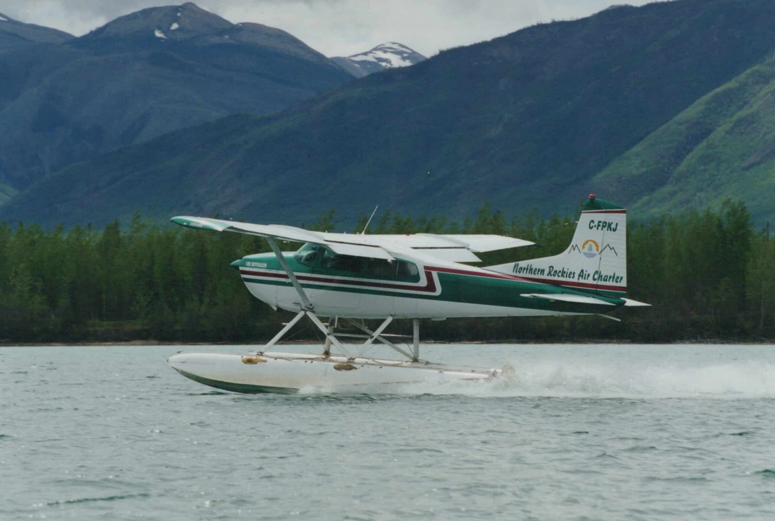 Seaplane launching from the lake at Scoop Lake Outfitters, surrounded by lush green mountains.